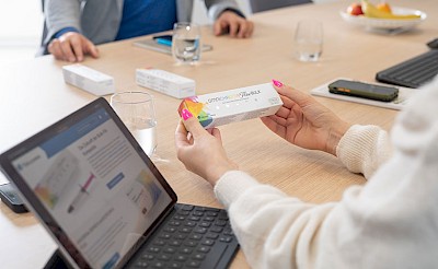 Laptop mit Tokuyama-Website und Hände, die das Produkt Omnichroma, in der Hand halten zur Veranschaulichung der Tätigkeit als Vertriebsassistenz (m/w/d) bei Tokuyama